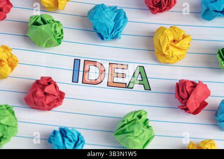 Idee. Das Wort Idee auf Notizblock geschrieben mit ein paar bunten zerknitterten Papierkugeln. Nahaufnahme. Stockfoto