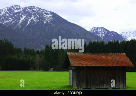 Berghaus auf einer grünen Wiese mit den Alpen im Hintergrund Stockfoto