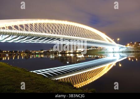 Hell beleuchtete moderne Brücke mit symmetrischer Reflexion im ruhigen Wasser während der Nacht in Prag, Tschechische Republik. Stockfoto