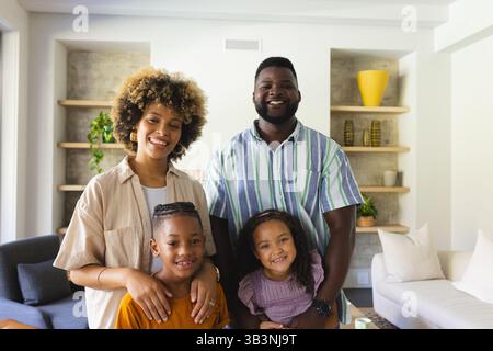 Lächelnde vierköpfige Familie posiert zusammen in einem hellen, modernen Wohnzimmer mit eingebauten Regalen Stockfoto
