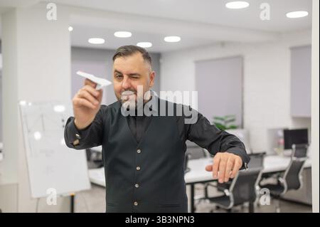 Kaukasischer bärtiger Mann, der Papierflugzeug im Büro abfeuert. Stockfoto