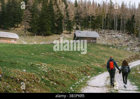 Planina podvežak, Slowenien 27.4,2025: Ein Paar spaziert auf einem gewundenen Pfad durch Planina Podvežak, Slowenien, umgeben von Holzhütten und zerklüfteter Alp Stockfoto