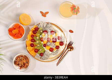 Obstsalat mit Weichkornkäse, Joghurt, Drachenfrucht, Kiwi, Mango, Orangen, Nüsse, Trauben und Saft, gesundes leichtes Frühstück mit Zutaten Stockfoto