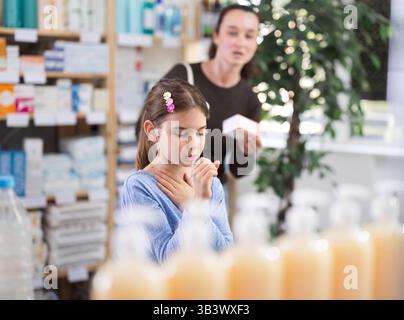 Das Kind steht und hustet in der Apotheke, und die Mutter wählt Medikamente Stockfoto