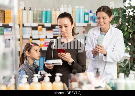 Frau, die telefonisch die Inhaltsstoffe der Salbe unter Anleitung des Apothekers überprüft Stockfoto