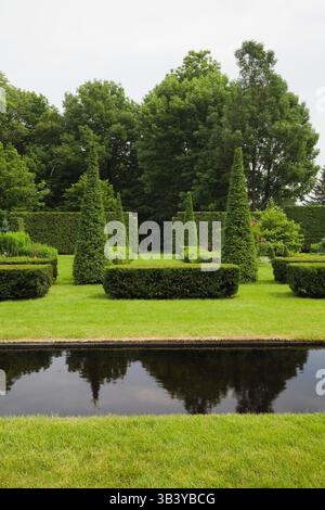 Gepflegter grüner Rasen mit italienischem Spiegelpool und abgeschnittenen Thuja - Zedernbäumen und Hecken im Garten im Sommer. Stockfoto
