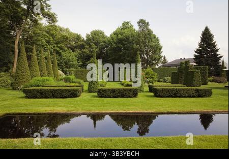 Gepflegter grüner Rasen mit italienischem Spiegelpool und abgeschnittenen Thuja - Zedernbäumen und Hecken im Garten im Sommer. Stockfoto