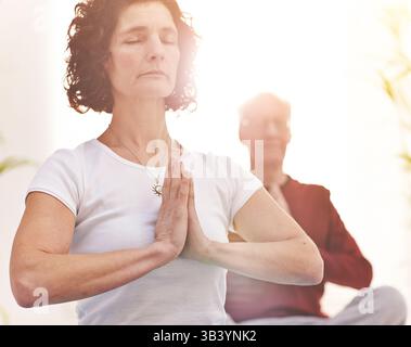 Seniorenpaar meditiert zusammen in einem Raum mit hellem Sonnenlicht. Ruhige und achtsame alte Frau und Mann, die Yoga mit der Sonne in der machen Stockfoto
