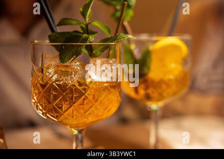 Zwei wunderschön gefertigte Cocktails sitzen auf einem Holztisch, garniert mit Minzzweigen und Zitronenscheiben. Die warme Atmosphäre deutet auf eine herrliche hin Stockfoto