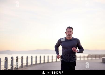 Strand, Laufen und Mann mit Herz-Kreislauf, Bewegung und Wellness mit Workout, Energie und Routine. Person, Athlet und Läufer mit Ausdauer, Fitness und Stockfoto