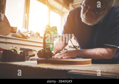 Erfahrener, kreativer und professioneller Zimmermann, der in einer Werkstatt Holzgitarre herstellt. Erfahrener Unternehmer, Handwerker, der ein Instrument während der Verwendung erstellt Stockfoto