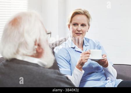 Pflegekraft, Pfleger und medizinisches Fachpersonal, das mit Rentner sitzt. Sprechende Krankenschwester, die sich mit Seniorin in Altersheim verbindet, zuhören Stockfoto
