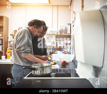 Kochen, Paare und Essen mit einem Seniorenpaar, das zusammen eine Mahlzeit in der Küche ihres Hauses zubereitete. Echte ältere Männer und Frauen machen einen Snack Stockfoto