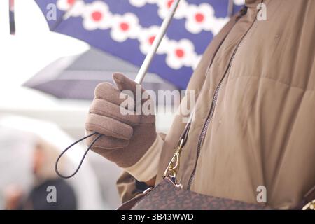 Hände halten einen Schirm bei regnerischem Wetter in einem überfüllten Bereich Stockfoto