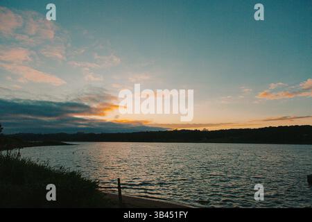 Sonnenaufgang über einem ruhigen See mit bunten Wolken und sanften Wellen auf dem Wasser. Stockfoto