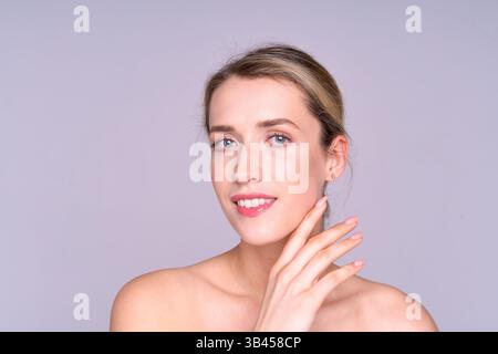 Junge Frau mit blauen Augen, die sanft die Wange berühren, mit gepflegter Haut auf hellem Hintergrund. Stockfoto