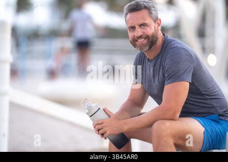 Sport-Fitness-Mann, der draußen auf einer Bank ruht. Reifes Fitnesssportmodell, das nach dem Training auf einer Bank sitzt. Ein Sportmann macht nach dem Fitnesstraining eine Pause Stockfoto