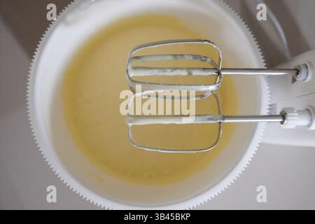 Zubereitung der Teigmischung in einer Schüssel mit beweglichem Mixer, Eiern, Milch, Teig, Wasser, Zutaten in Mischung, Nahaufnahme, kulinarische Aktivität. Stockfoto