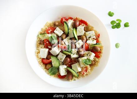 Couscous mit Feta und frischem Gemüse wie Tomaten, Gurken und Paprika, serviert in einer weißen Schüssel auf weißem Hintergrund.gesundes und vegetarisches Essen. Stockfoto