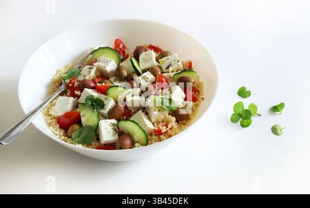 Couscous mit Feta und frischem Gemüse wie Tomaten, Gurken und Paprika, serviert in einer weißen Schüssel auf weißem Hintergrund. Gesunde und vegetarische Lebensmittel. Stockfoto