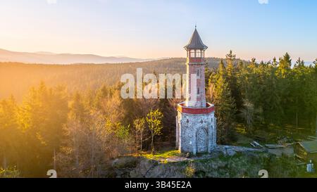 Der Stepanka Aussichtsturm steht hoch im Isergebirge an einem ruhigen Frühlingsmorgen. Die umliegenden Bäume sonnen sich im warmen Sonnenlicht und schaffen eine ruhige, natürliche Umgebung. Stockfoto