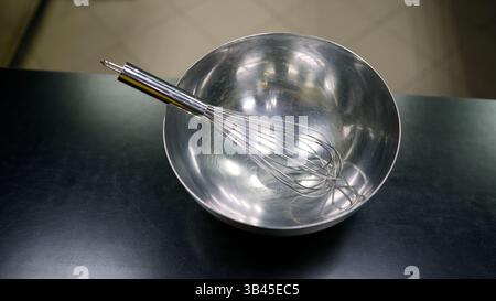 Metallquirl in einer Edelstahlrührschüssel auf schwarzer Arbeitsplatte, bereit zum Kochen und Backen Stockfoto