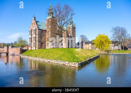 Schloss Rosenborg steht majestätisch auf seiner Insel, umgeben von ruhigen Gewässern in Kopenhagen. Der klare blaue Himmel unterstreicht die historische Architektur des Schlosses und schafft einen malerischen Blick. Stockfoto