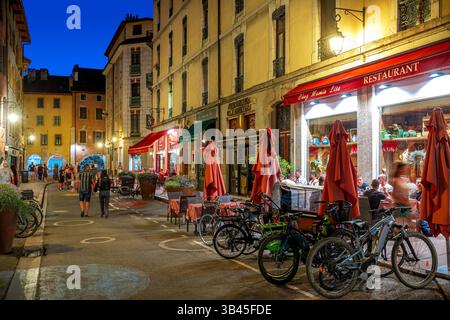 Abends schlendern die Menschen entlang der Straße mit beleuchteten Bars und Restaurants in der Altstadt von Annecy, Frankreich. Stockfoto