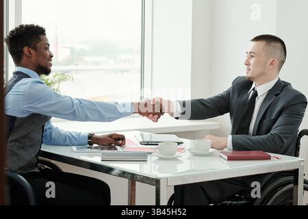 Zwei junge interkulturelle Geschäftspartner schütteln sich nach der Verhandlung die Hand Stockfoto