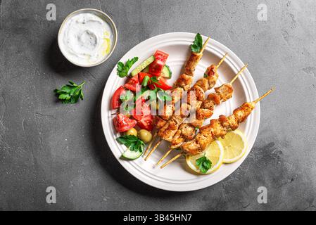 Gegrillte Hähnchenkebabs mit frischem Gemüsesalat auf Teller, Draufsicht, Kopierraum. Mediterranes Keto-Mittagessen mit gebratenen Fleischspießen, Tzatziki-Sauce A Stockfoto