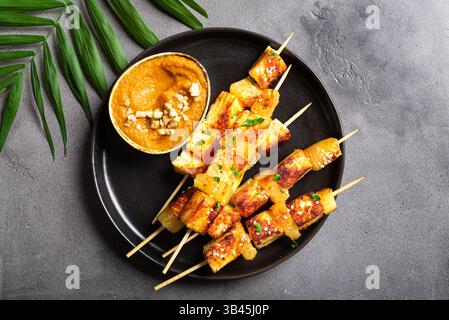 Gegrillter Tofu- und Ananassatay-Spieß mit würziger Erdnusssauce auf grauem Betonhintergrund, Draufsicht, Kopierraum. Gebratene halloumi-Käsekebabs. Vegan Stockfoto