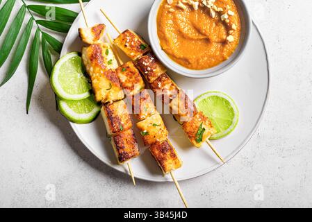 Gegrillte Tofu Satay Spieße und Erdnusswürzsauce auf weißem Teller in Nahaufnahme... Asiatisches veganes vegetarisches Mittagessen, thailändische Gerichte. Stockfoto