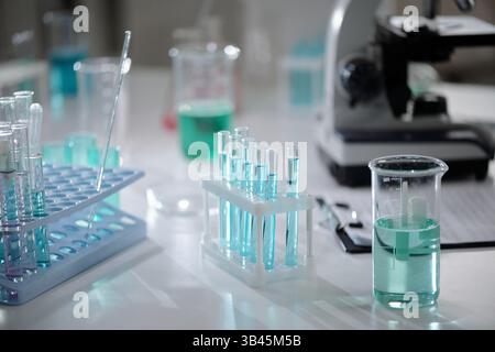Labortisch mit verschiedenen Bechergläsern, Reagenzgläsern und einem Mikroskop im Fokus. Vorhandensein chemischer Lösungen in Behältern, Hinweis auf laufende Experimente Stockfoto