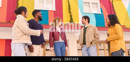Gruppe multiethnischer junger Studenten, die sich vor einer bunten Regenbogenwand unterhalten und lächeln und ihre Pausen im Freien genießen Stockfoto