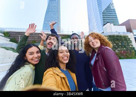Gruppe fröhlicher, multiethnischer Freunde, die Selfie machen und vor Wolkenkratzern vor der Kamera winken Stockfoto