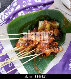 Indonesischer Sate oder Ayam Chicken Satay mit Lontong-Reiskuchen und Erdnusssauce serviert auf einem Bananenblatt zum Mitnehmen. Stockfoto