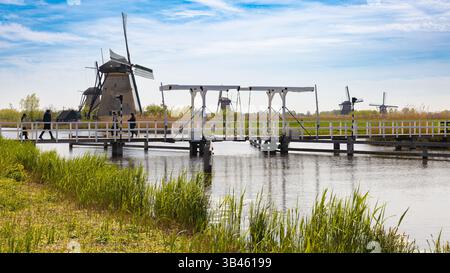 Panoramablick auf Kinderdijk, Niederlande, mit historischen Windmühlen, einer Brücke über einen Wasserweg mit Menschen, die überqueren, und lebendiger grüner Landschaft un Stockfoto