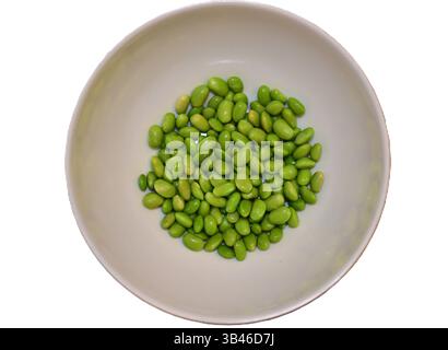 Eine halbe leere Schüssel mit grünen Bohnen isoliert auf der weißen Ebene von oben. Frische, glänzende Edamambohnen in einer weißen Schüssel. Stockfoto