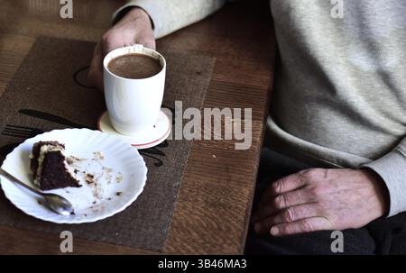 Die Hände der älteren Männer porträtieren Kaffee trinken und Kuchen essen. Seniorenmann Hände aus nächster Nähe. Zerknitterte Hände trinken Kaffee. Stockfoto