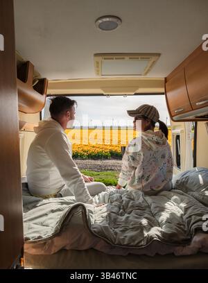 Ein Paar entspannt sich in ihrem Wohnmobil und bestaunt atemberaubende Tulpenfelder in Flevoland, Niederlande. Die goldenen Blüten erstrecken sich endlos und fangen die Freude an Frühlingsabenteuer ein. Stockfoto