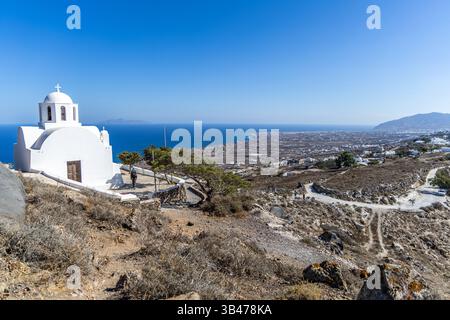 Santorin, Griechenland - 15. Oktober 2024: Weiß getünchte griechische Kirche mit Blick auf das Blaue Meer und die Berge auf der Insel Santorin. St. Markus Heilig-Orthodoxe Kapelle. Stockfoto