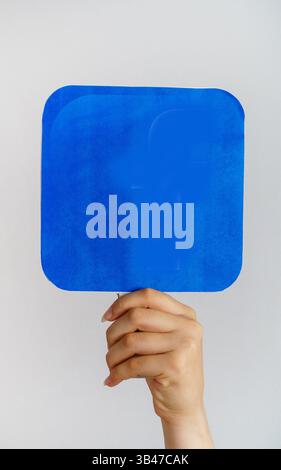 Weibliche Hand mit leerem, nachgeahmtem Banner als Kopierraum für Zitatstexte oder Grafikdesign. Blaues Quadrat in weiblicher Hand auf grauem Hintergrund. Stockfoto