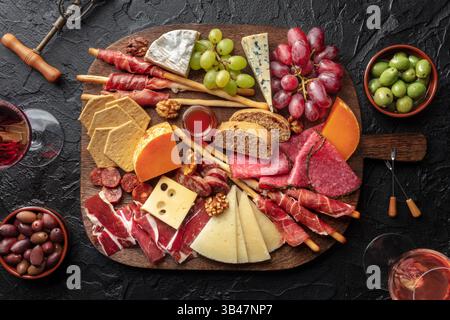 Antipasti oder Tapas. Wurst- und Käseplatte mit Wein, von oben auf einem schwarzen Tisch geschossen. Italienische oder spanische Speisen und Getränke Stockfoto