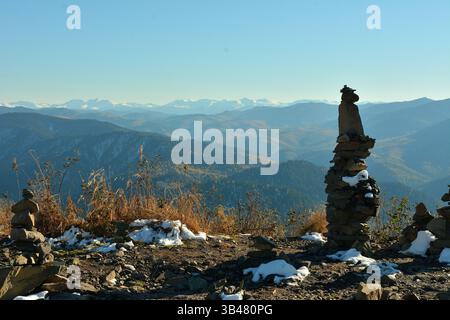 Eine hohe Steinpyramide bedeckt mit dem ersten Schnee auf einem Berg mit Blick auf ein malerisches Tal an einem sonnigen Herbstabend. Berg Kokuya, Altai, Stockfoto