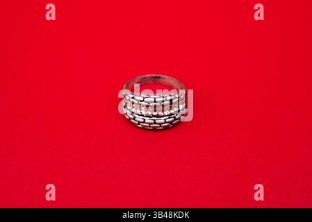 Ein luxuriöser Silberring mit einem hellen Edelstein, der vor rotem Hintergrund seinen Glanz und seine komplizierten Details unterstreicht. Stockfoto