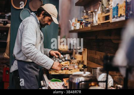 Person, die Speisen in einer gemütlichen Küche mit einer Vielzahl von Zutaten zubereitete Stockfoto
