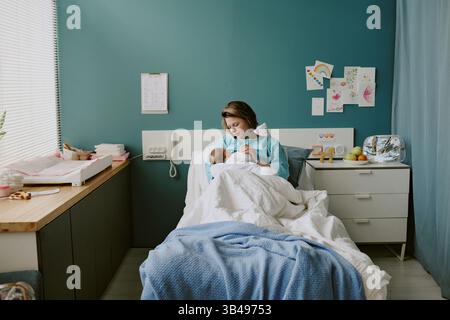 Krankenschwester hält Neugeborenes im Krankenhauszimmer gefüllt mit medizinischen Geräten und bunten Dekorationen an der Wand Stockfoto
