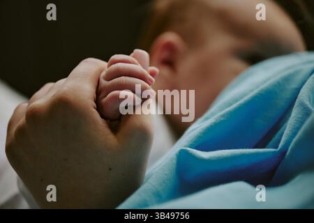 Nahaufnahme mit der Hand eines Erwachsenen, die sanft die Hand eines Babys hält. Sanft beleuchtete Szene zeigt Berührung und Verbindung zwischen Kind und Elternteil Stockfoto