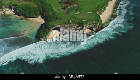 Atemberaubende Aussicht aus der Luft mit türkisfarbenen Wellen, die gegen Klippen und Sandstrände des Pantai Dreamland Beach prallen, neben einem üppig grünen Golfplatz in Bali, Indonesien Stockfoto