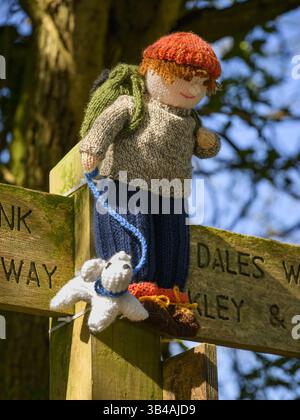 Yarnbombe Person am Fingerpfosten befestigt (öffentlicher Fernwanderweg, Ebor Way, Dales Way Link) Nahaufnahme - Menston, West Yorkshire, England Großbritannien. Stockfoto